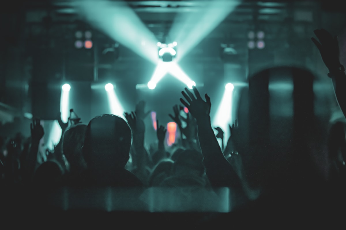 Crowd with hands raised on a nightclub dance floor under stage lights