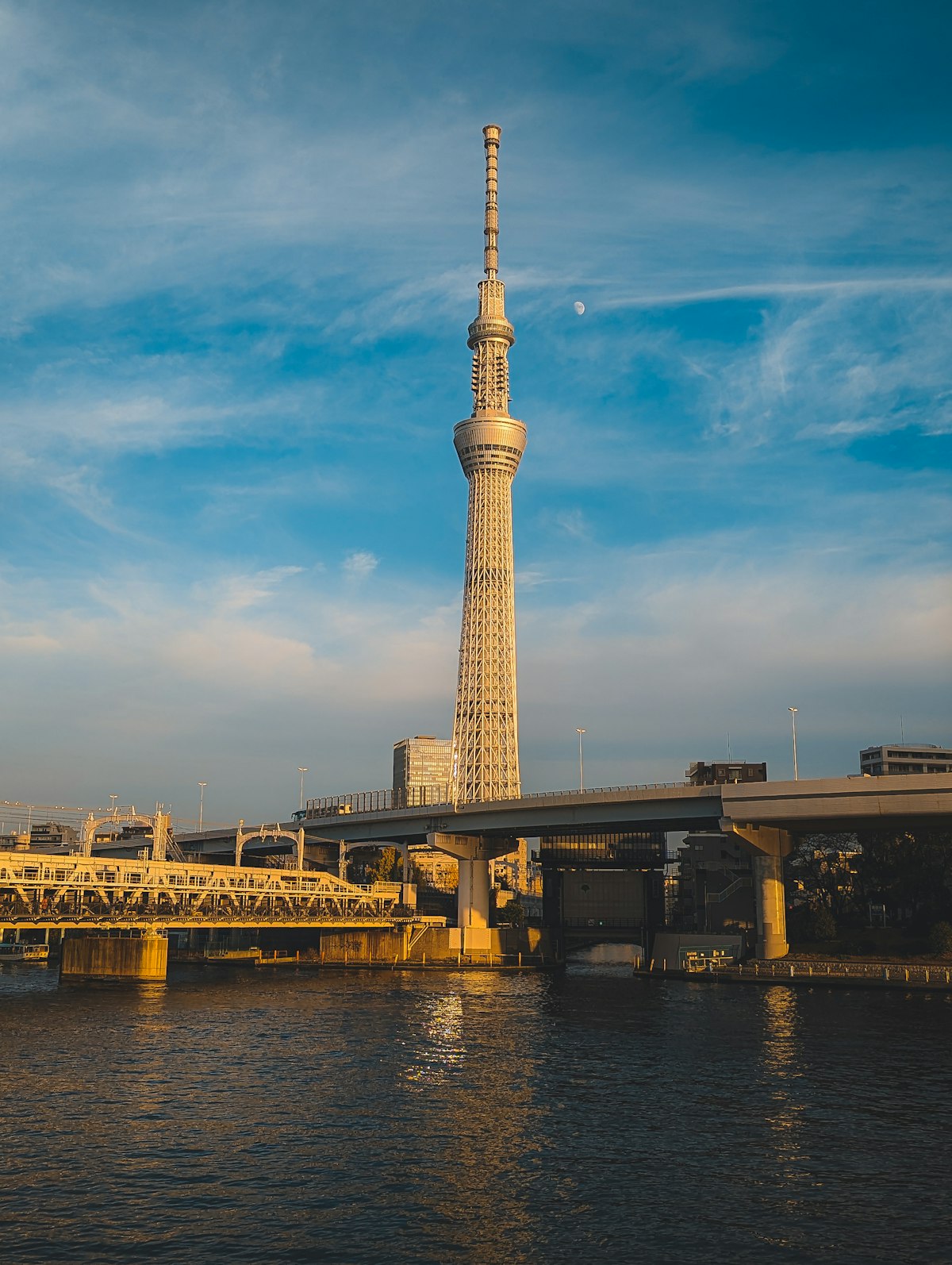Tokyo Skytree illuminated at night towering over the Sumida River next to a bridge, seen from the Asakusa side