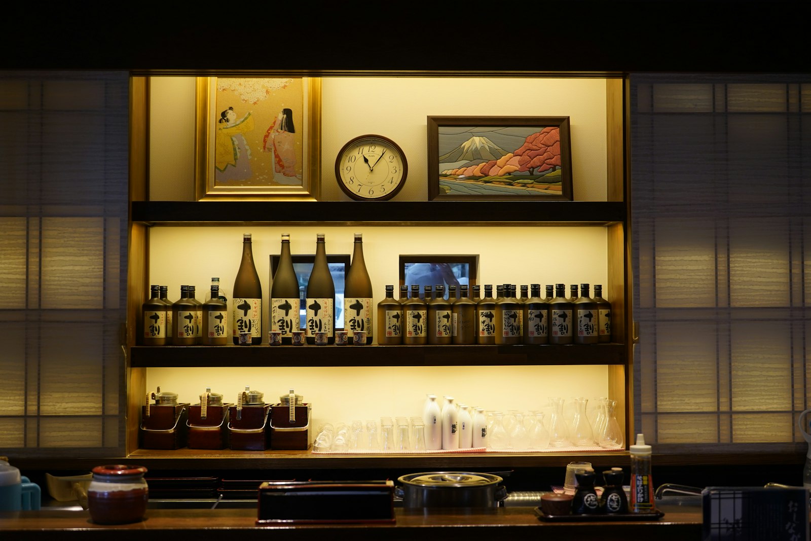 A narrow Japanese bar counter lined with bottles and glasses under warm lighting, the typical layout of a Tokyo girls bar