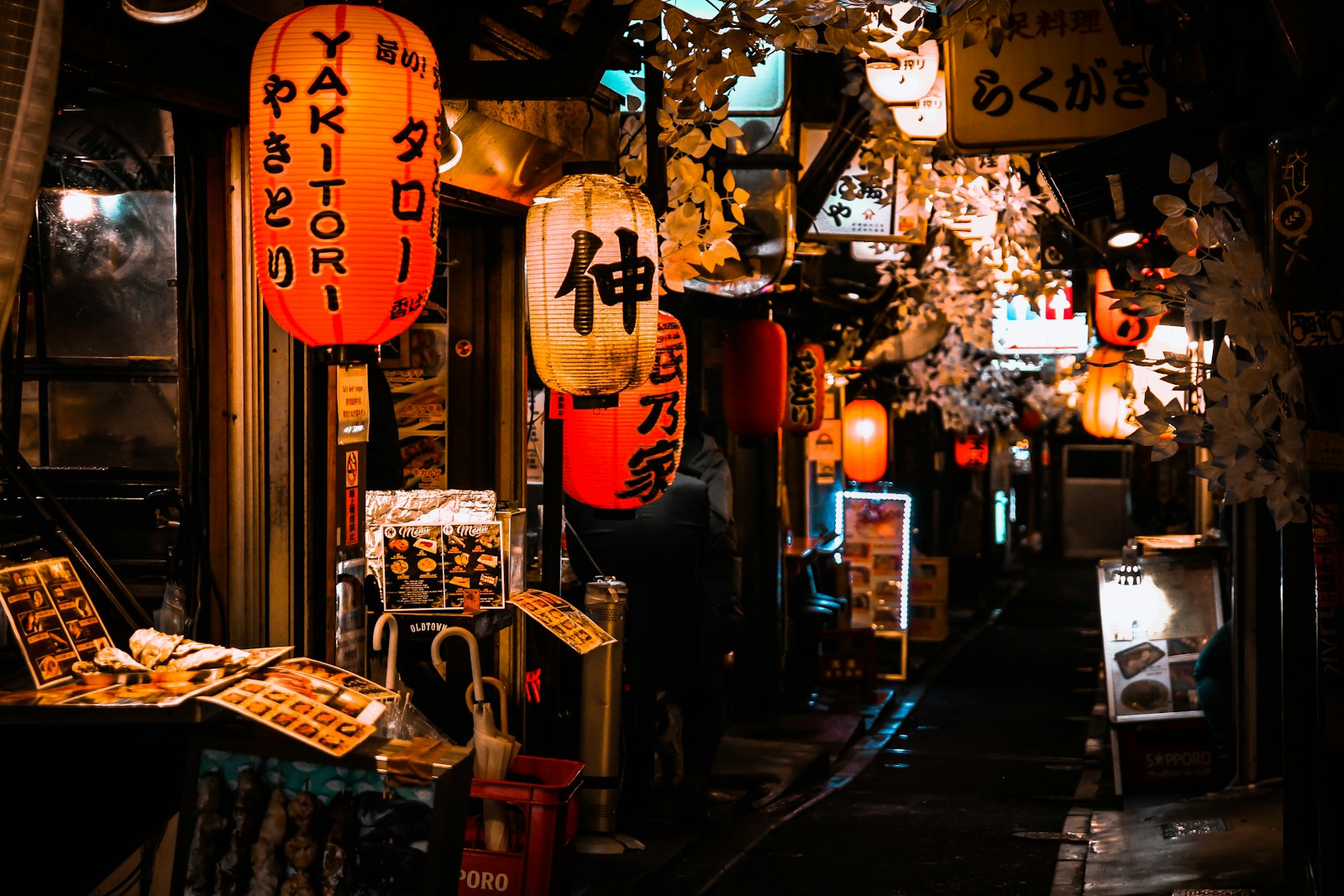 A narrow Tokyo backstreet at night lined with small bars and glowing lanterns