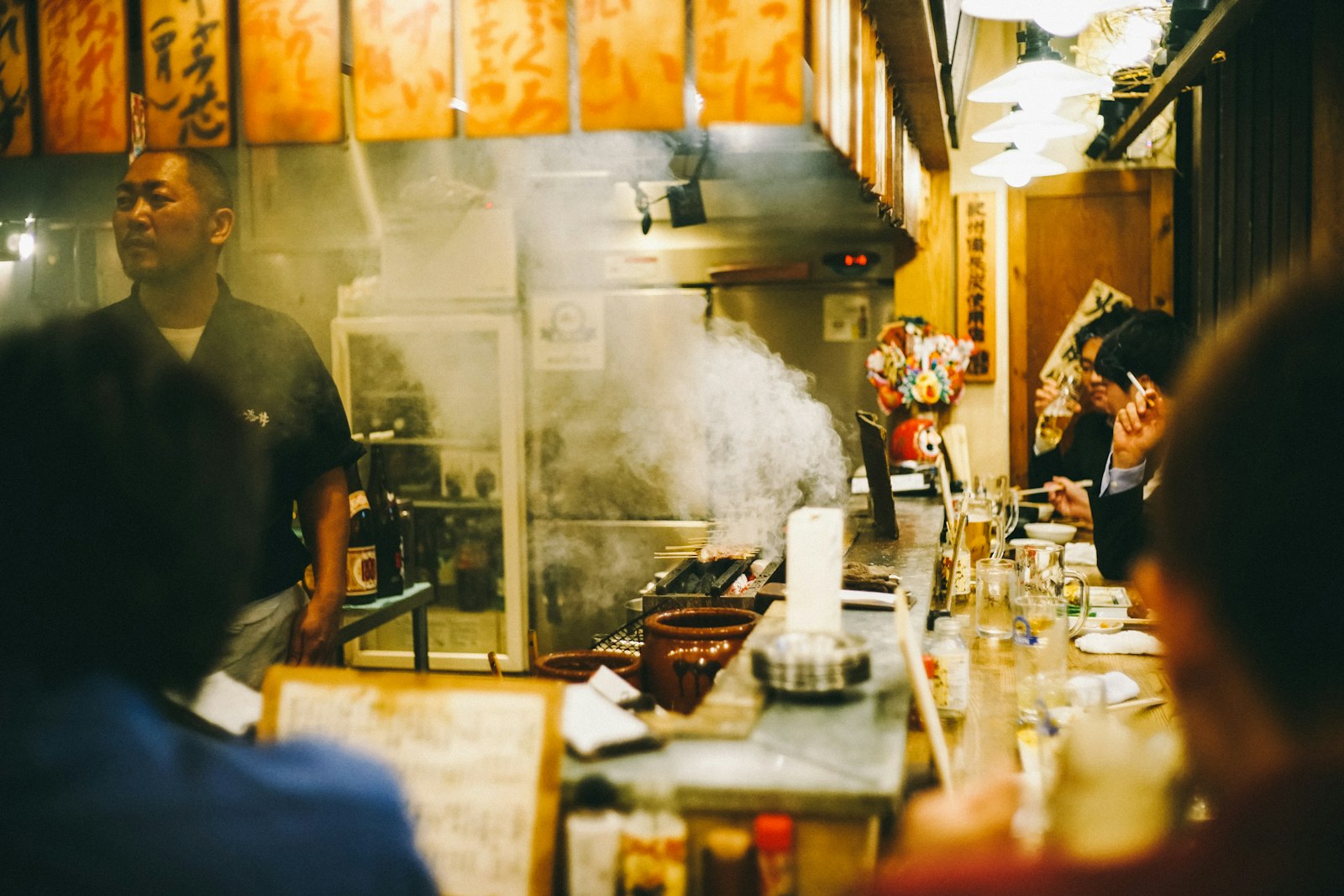 Chef grilling yakitori skewers over charcoal at a tiny counter izakaya in a Tokyo yokocho
