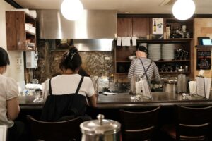 A bartender working behind the counter of a small Japanese bar at night, where you'll order your first drink