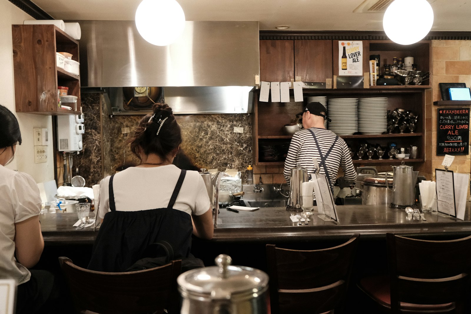 A bartender working behind the counter of a small Japanese bar at night, where you'll order your first drink