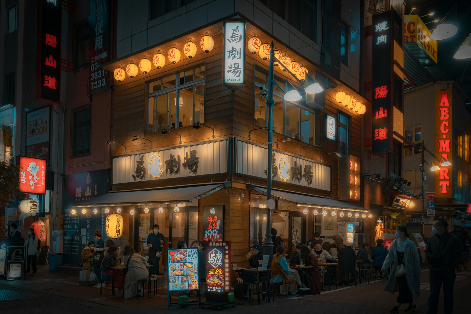 Visitors at the counter of a small Tokyo izakaya with a menu on the wall