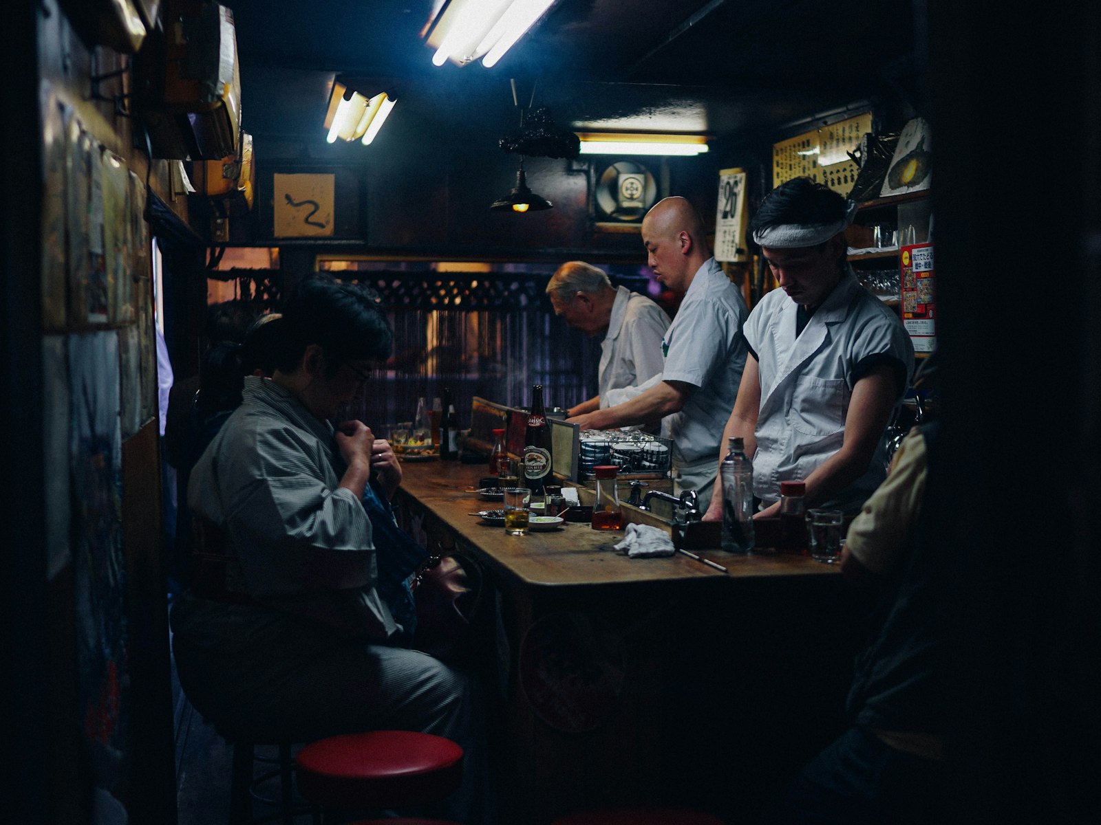 Customers drinking and eating at a crowded Tokyo izakaya counter at night