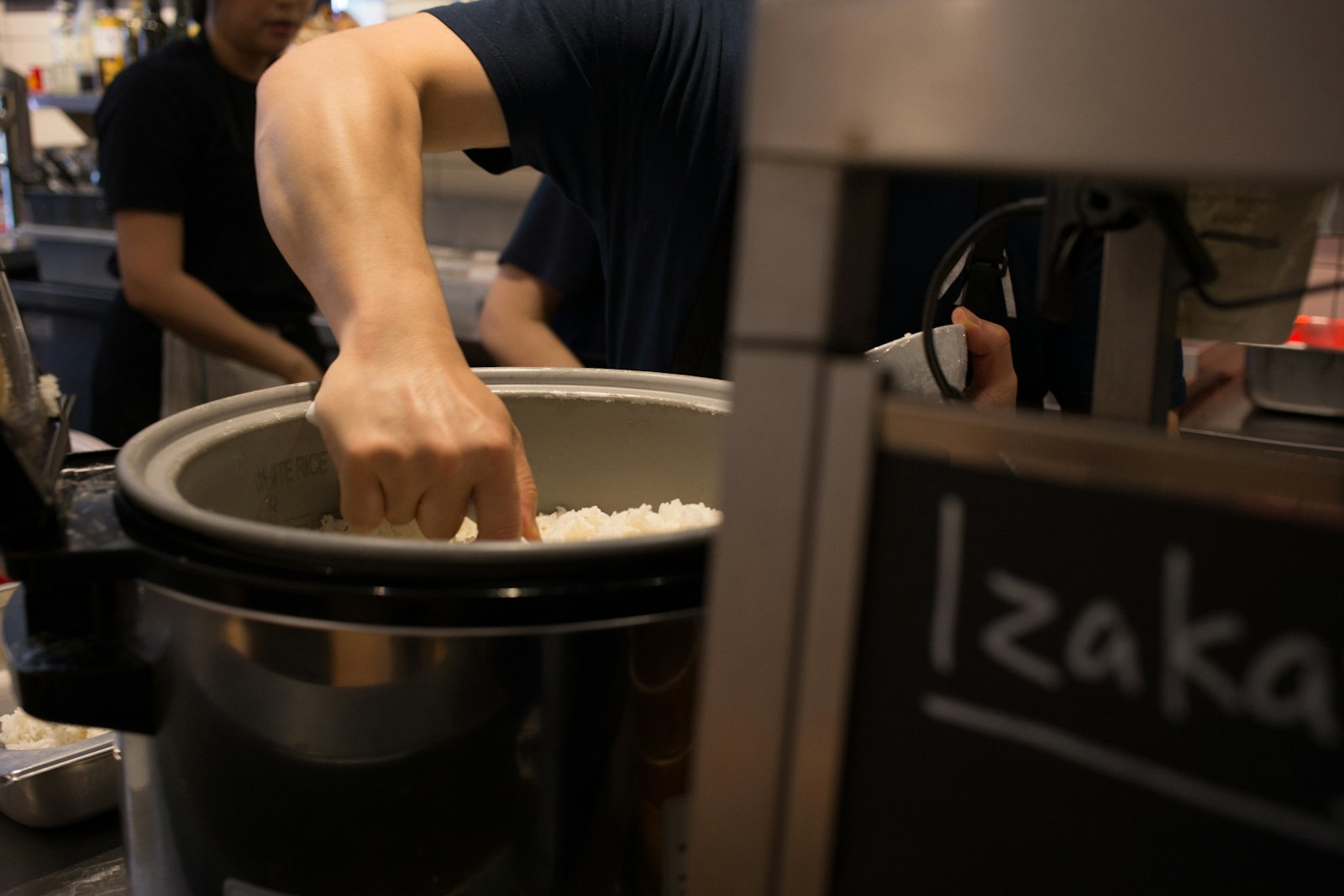 Pouring warm sake from a tokkuri into a small ochoko cup at an izakaya counter