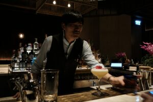 A Japanese bartender stirring a cocktail behind a wooden counter at a Tokyo cocktail bar