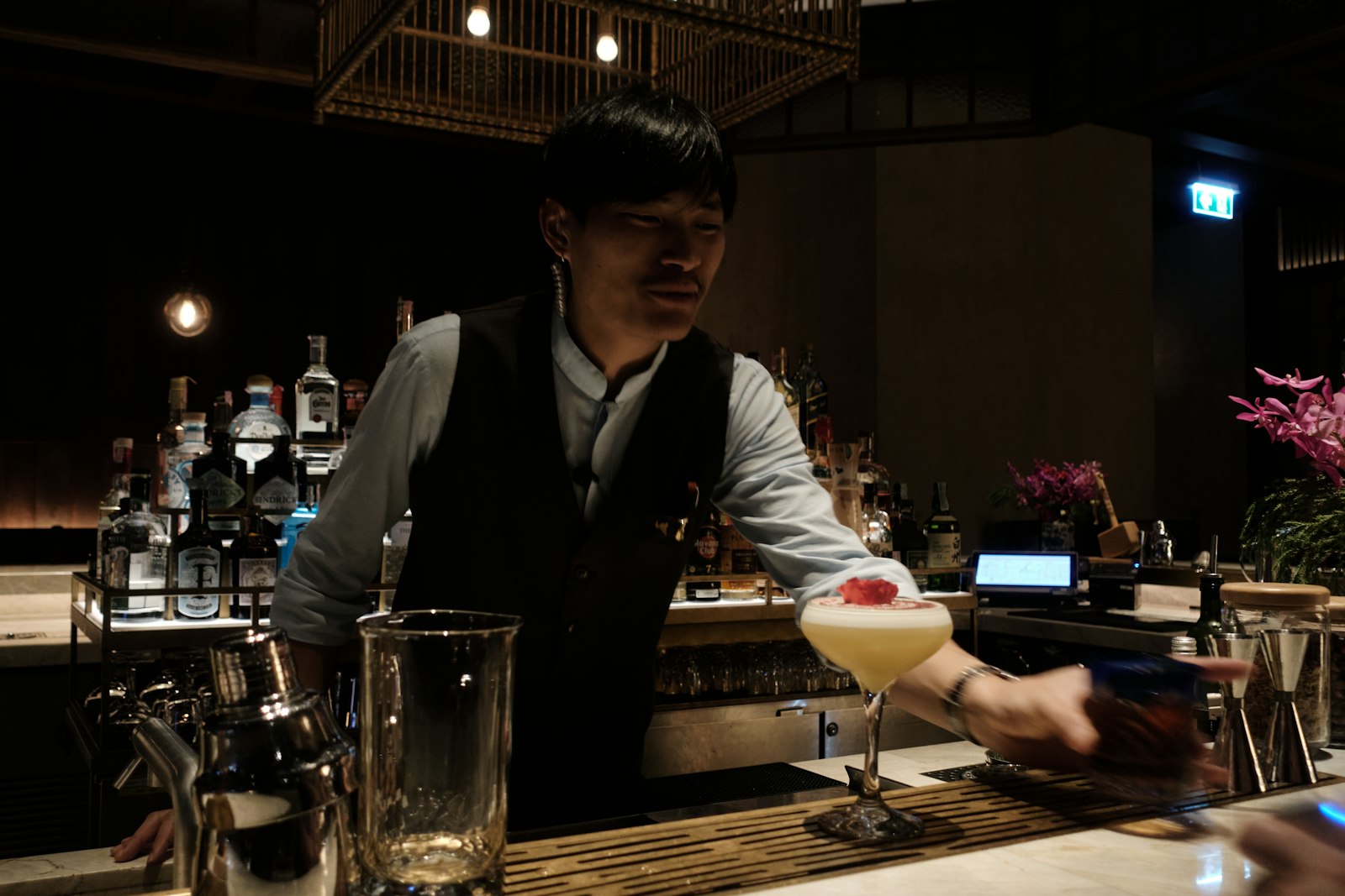 A Japanese bartender stirring a cocktail behind a wooden counter at a Tokyo cocktail bar