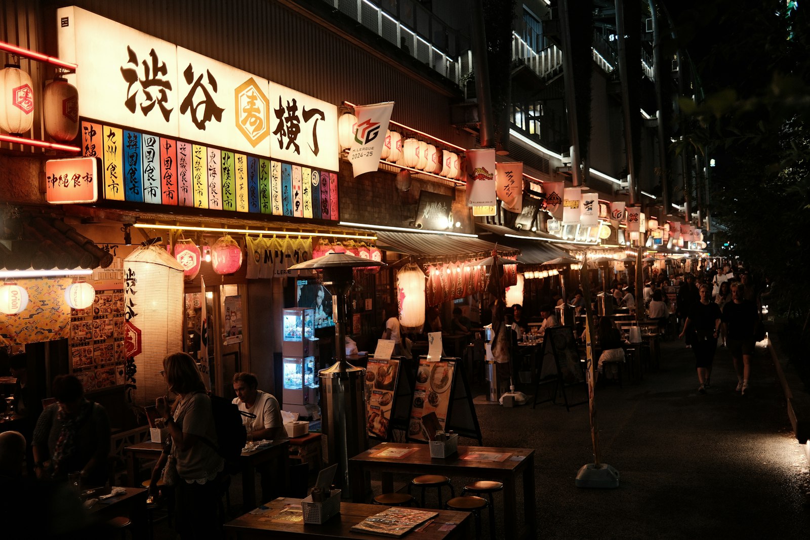 Locals sharing beer and yakitori at a small counter in a Tokyo alley at night
