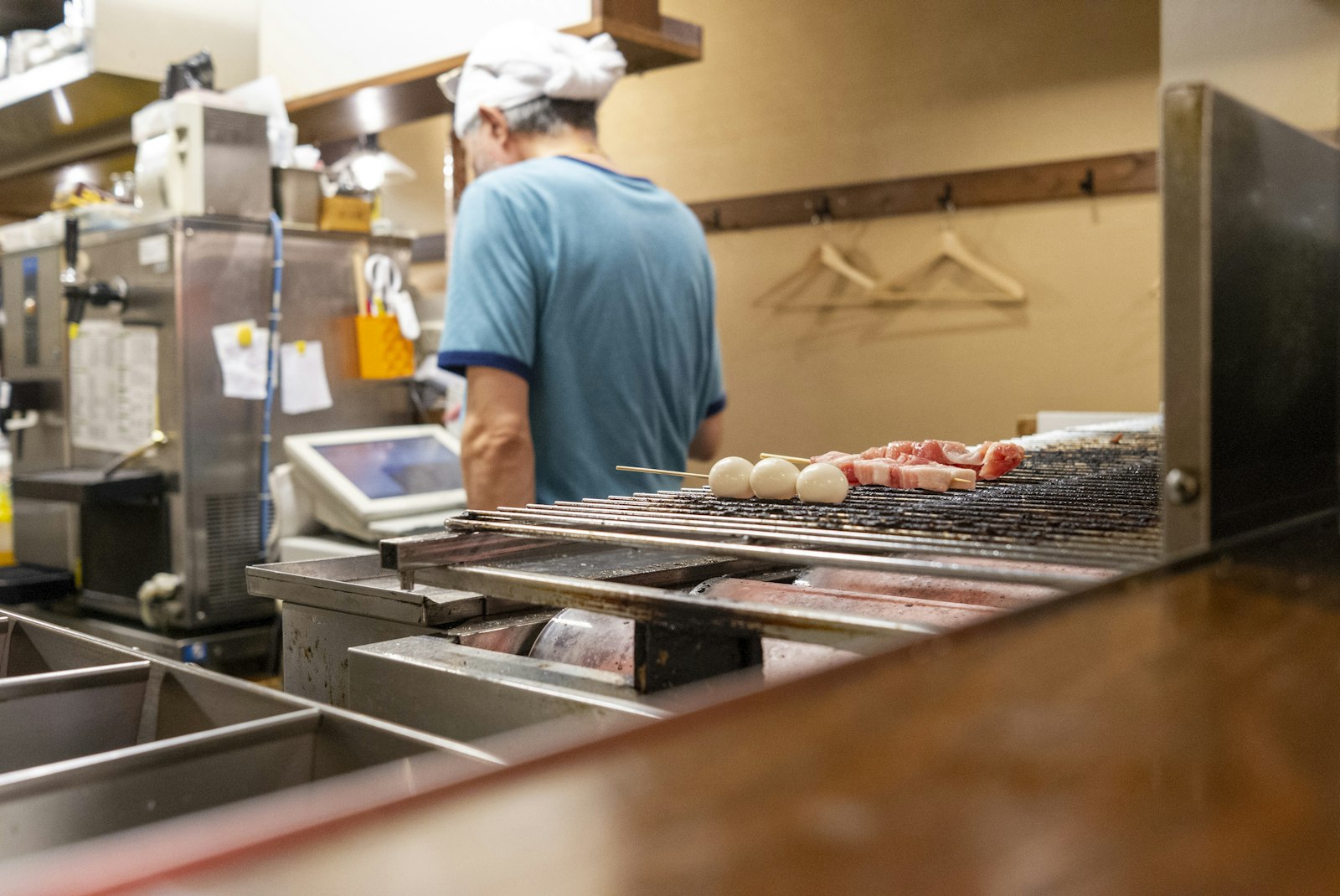 Chef grilling yakitori skewers behind a tiny counter at a Tokyo izakaya, the standard setup in a yokocho alley bar