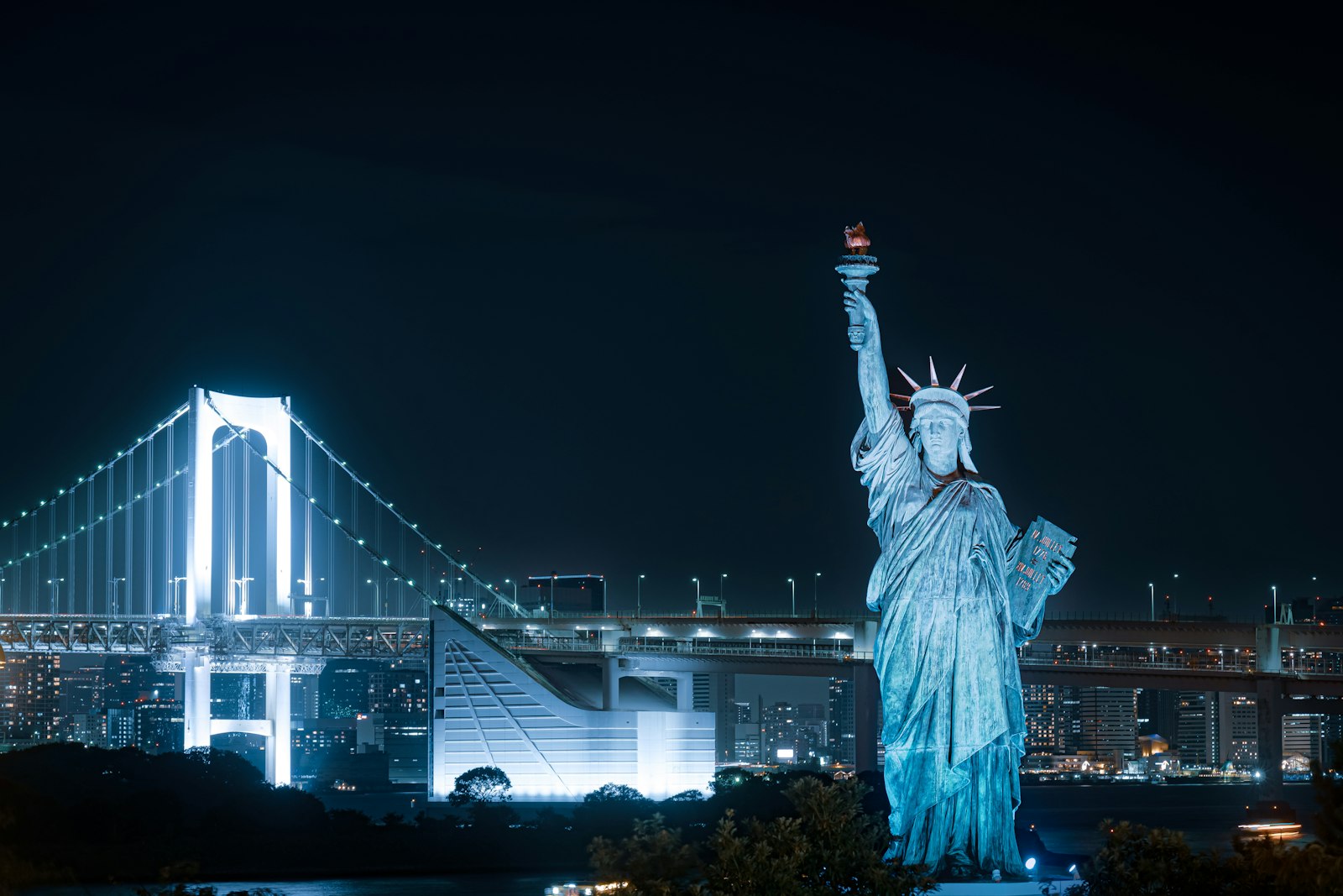 Statue of Liberty replica in Odaiba Seaside Park with the illuminated Rainbow Bridge behind it at night