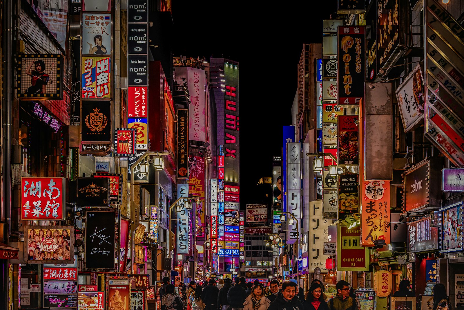 Neon signs stacked above a crowded street in Shinjuku at night, a classic Tokyo street photography scene
