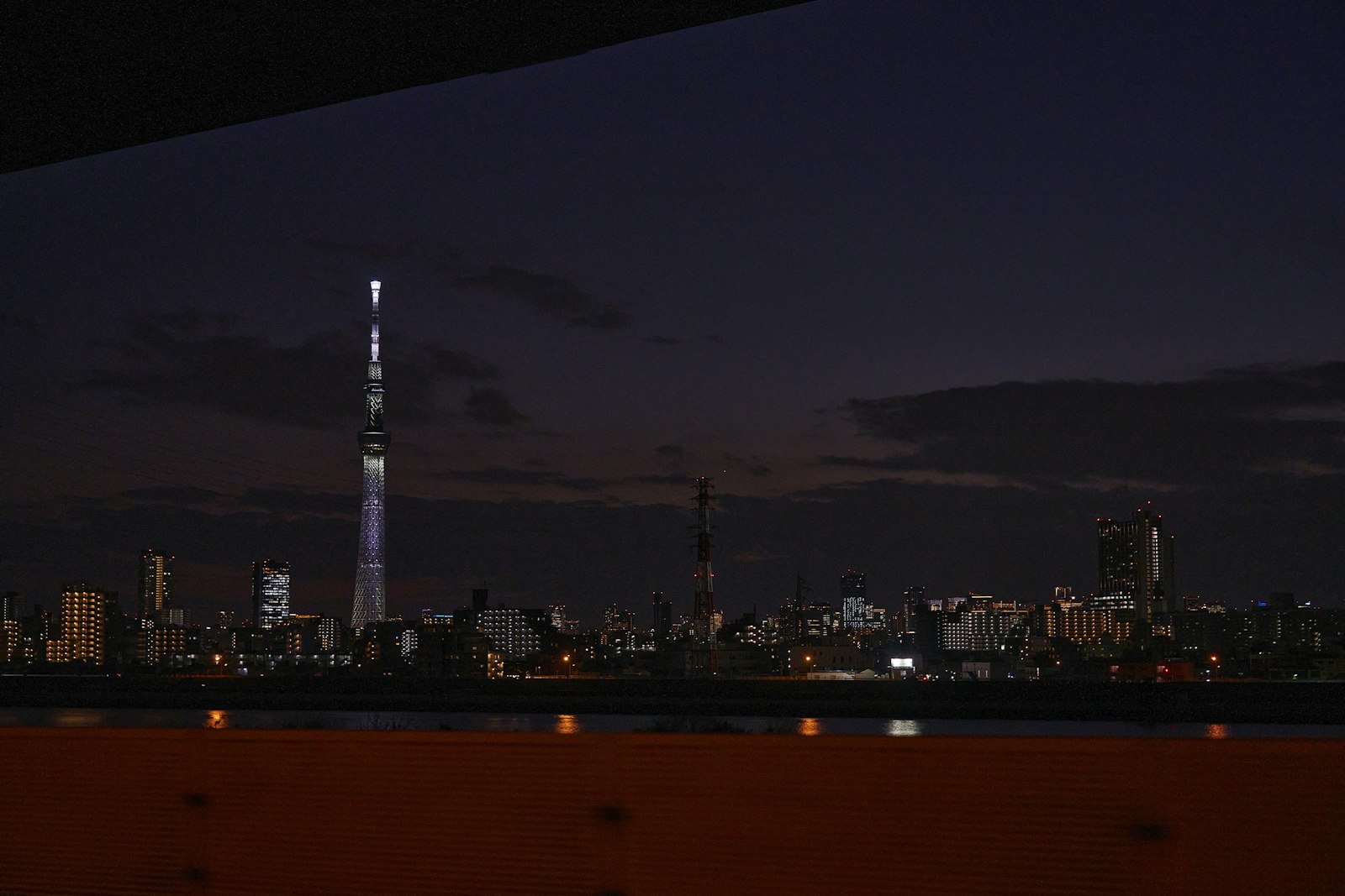 Tokyo Skytree reflected in the river at night, lit in pale blue